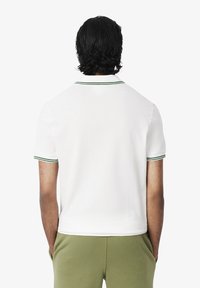 Polo shirt blanc avec col et accents de manches verts, fabriqué en coton, avec des manches courtes et une coupe classique. Texture lisse.