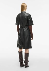 Juodas odinis sijonas su trumpomis rankovėmis, diržu liemenyje ir užpakaline skyle. Derinamas su rudiems iki kelių aukštakulniais batais. Lygus audinys ir prigludusi forma.