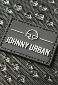 Szary, teksturowany materiał z błyszczącymi, dekoracyjnymi kropkami; zawiera szary tłoczony metek z napisem "JOHNNY URBAN" oraz minimalistyczny wzór logo.