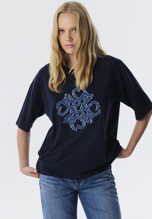 Marineblauw oversized t-shirt van katoen, met een versleten denim logo ontwerp in het midden van de voorkant. Korte mouwen en een relaxed fit.