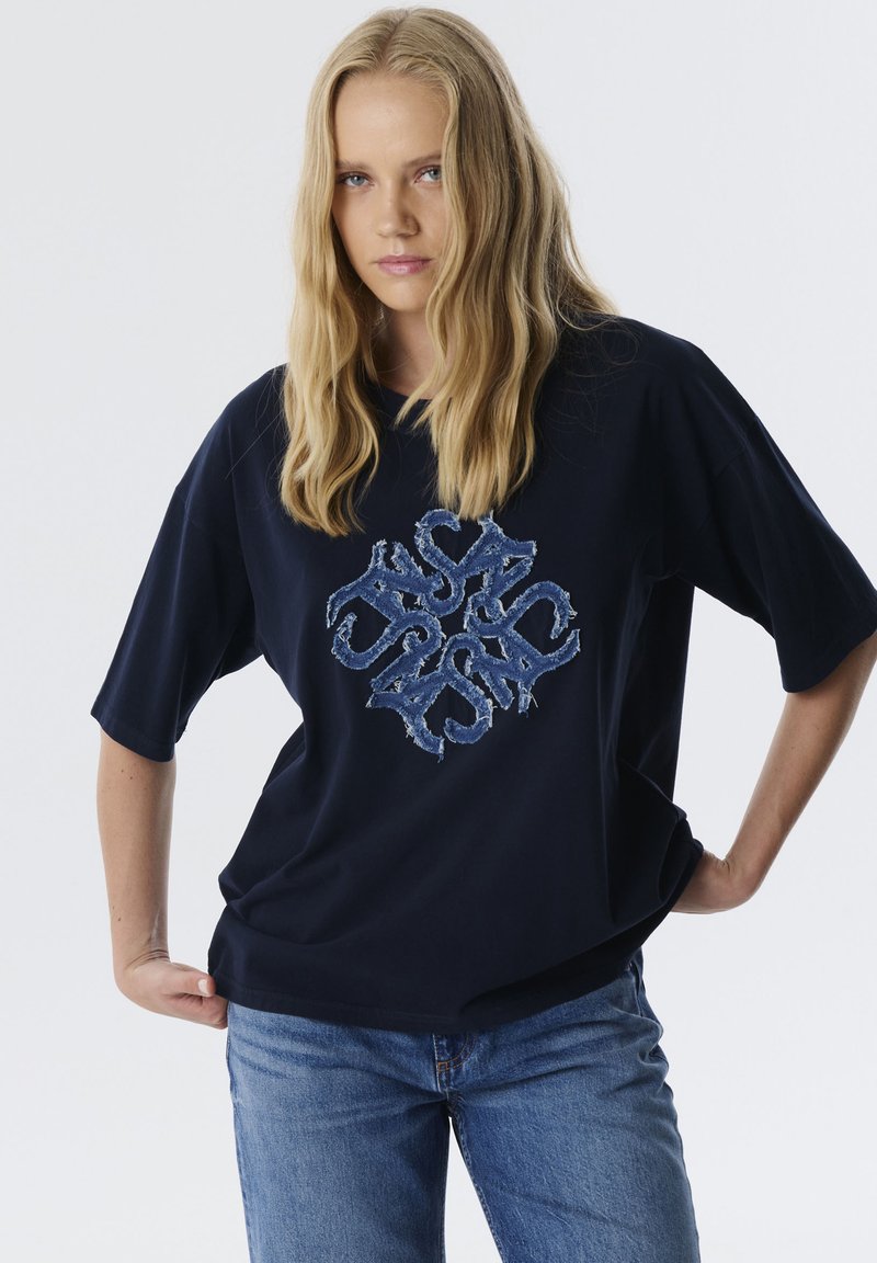 Marineblauw oversized t-shirt van katoen, met een versleten denim logo ontwerp in het midden van de voorkant. Korte mouwen en een relaxed fit.