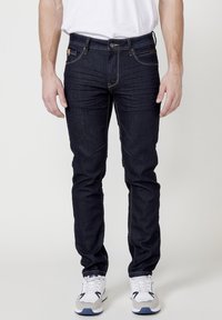 Dunkelblaue Jeans mit Slim-Fit, aus Denim gefertigt. Mit sichtbaren Nähten, fünf Taschen-Design und Messingbeschlägen für den Verschluss.
