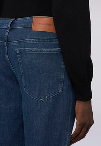 Jeans in denim blu scuro con superficie texturizzata, caratterizzati da un'etichetta in pelle Trussardi sulla vita e tasche posteriori standard.