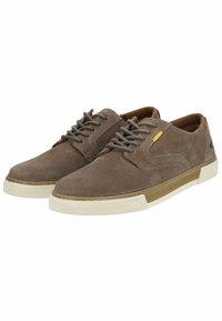 Zapatillas de ante marrón con un acabado texturizado, que cuentan con una suela de goma blanca y detalles en marrón. Cordones y un pequeño detalle amarillo cerca de los ojales.