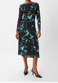 Schwarzes Langarmkleid mit türkisfarbenem und lila abstraktem Muster, tailliert, aus durchsichtigem Stoff, kombiniert mit schwarzen Absätzen.