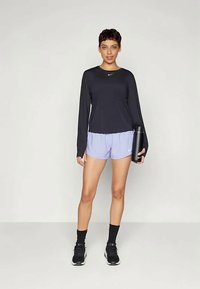 Fekete hosszúujjú sportfelső, levendula rövidnadrág, fekete edzőcipő, fekete vízpalack. Simább anyag, kerek nyakkivágás, testhezálló fazon, logós részlet.