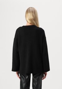 Svart oversized genser med ribbestrikket kant og mansjetter, laget av et mykt teksturert materiale, sett fra baksiden.