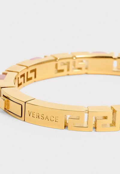 Βραχιόλι Versace με χρυσή απόχρωση, σχέδιο ελληνικού κλειδιού και χαραγμένο όνομα της μάρκας σε λείες ορθογώνιες πέρλες.