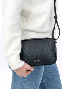 Borsa a tracolla nera in pelle con superficie strutturata, forma rettangolare sottile, tracolla rimovibile e logo argentato discreto in basso.
