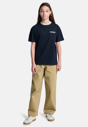 Zwarte katoenen t-shirt met "ELEMENT" logo, gecombineerd met losse kaki broeken en witte sneakers met bruine zolen. Eenvoudig, casual ontwerp.