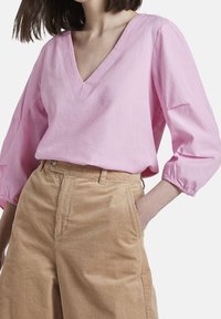 Blusa rosa con scollo a V e maniche a palloncino, abbinata a pantaloni in corduroy alta vita color marrone chiaro, con gambe ampie e tasche laterali.