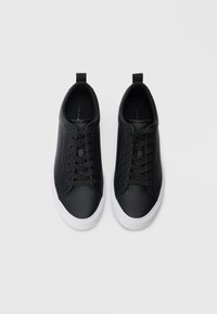 Μαύρα αθλητικά παπούτσια με λείο δερμάτινο επάνω μέρος, λευκή ελαστική σόλα και κλείσιμο με κορδόνια. Διαθέτει θηλιά στο πίσω μέρος και διακριτική επωνυμία στο πλάι.