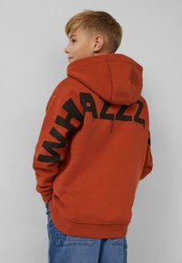 Sweatshirt à capuche orange avec un grand texte noir "WHALLZ" au dos. Fabriqué en tissu doux, avec des poignets et un ourlet côtelés ; coupe décontractée.