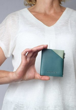 Tarnfarbenes Lederportemonnaie mit einer diagonalen, hellgrünen Akzentfarbe, ausgestattet mit einem silbernen Reißverschluss und einer geprägten Markenlogo auf der Vorderseite. Kompakte rechteckige Form.