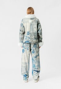 Chaqueta de mezclilla y pantalones a juego en una paleta de colores azul claro y beige con un patrón abstracto texturizado; presenta un cuello y puños de piel sintética blanca.