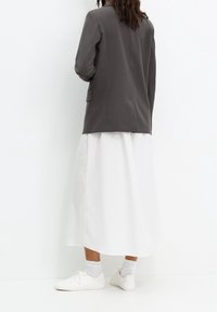 Blazer gris, jupe midi blanche et baskets blanches. Le blazer présente une texture lisse, une poche simple et une coupe ajustée.