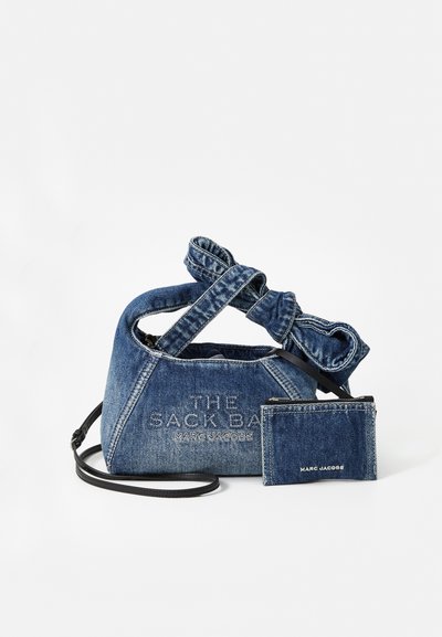 Sac en denim avec une forme arrondie, une bandoulière nouée et une marque en relief. Comprend un porte-cartes assorti en denim avec un accent noir.