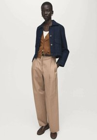 Blauwe spijkerjasje met een kraag, bruin overhemd met knopen, en beige wijduitlopende broek, gecombineerd met donkerbruine schoenen. Vlakke textuur, op maat gemaakte pasvorm.