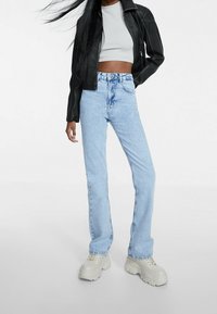 Chaqueta de cuero negra corta sobre una blusa gris, combinada con jeans rectos de mezclilla azul claro y zapatillas gruesas beige.