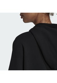 Il hoodie nero presenta una vestibilità rilassata con scollatura rotonda e cappuccio con cordino. Texture del tessuto liscia e dettagli di cucitura minimi.