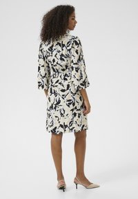 Abito a fantasia floreale con maniche 3/4; base crema, dettagli neri e blu; vita elasticizzata. Abbinato a scarpe con tacco beige.
