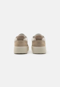 Sneakers with a beige suede upper and light cream leather accents, featuring a thick off-white sole. Minimalist design with rounded edges.