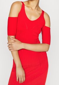 Robe rouge côtelée avec découpes aux épaules, dotée d'un col rond et de manches courtes ajustées. Le tissu a une texture lisse et un ajustement près du corps.