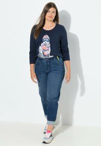 Camiseta de manga larga azul marino con un gráfico colorido de un perro, combinada con vaqueros azules. Calzado: zapatillas deportivas en gris, rosa y blanco.