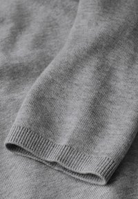 Grauer Strickpullover mit weicher Textur, der über ein geripptes Bündchen und einen glatten Körper verfügt und ein einfaches, klassisches Design betont.