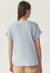 Top azzurro chiaro a maniche corte realizzato in un tessuto testurizzato, con maniche arrotolate e spacchi laterali, e un semplice design sul retro.