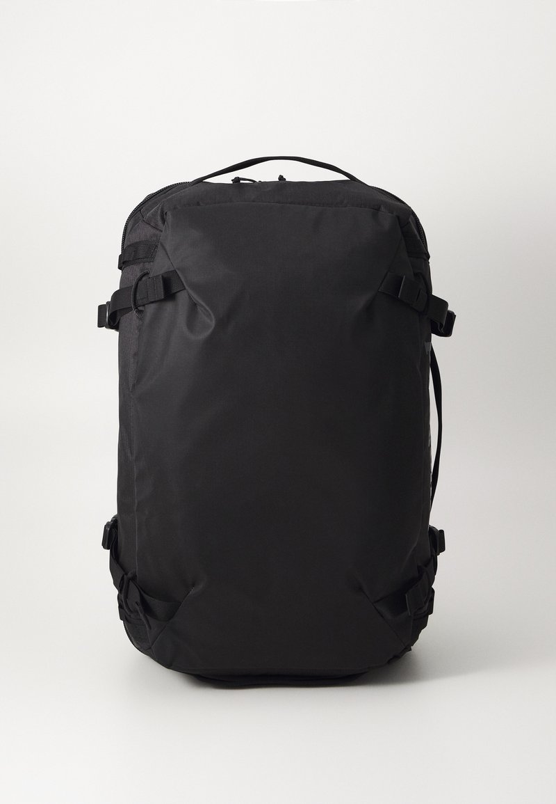 Mochila preta feita de tecido durável, com alças ajustáveis e fivelas. Apresenta uma textura suave e forma retangular.