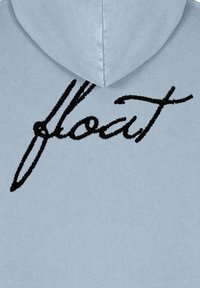 Sudadera azul claro con el texto bordado en negro "flout" en la parte trasera, con un acabado texturizado y diseño con capucha.