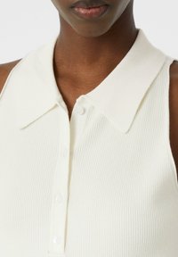 Gestreifter, ärmelloser Oberteil in Off-White mit klassischem Kragen und Knopfverschluss. Verfügt über einen strukturierten Stoff für zusätzlichen Detailreichtum.