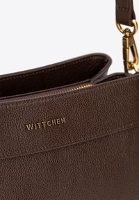 Brązowa torba ze strukturalnej skóry z złotym logo "WITTCHEN", zapinana na zamek błyskawiczny, z odpinanym paskiem. Widoczne subtelne detale przeszycia.