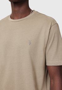 Beige cotton t-shirt with a crew neckline, short sleeves, and a small embroidered goat skull detail on the left chest. Smooth texture.