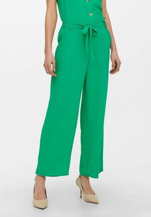 Grüne Hosen mit weitem Bein aus leichtem Stoff, mit gebundener Taille und Seitentaschen, kombiniert mit beigen High-Heel-Schuhen.