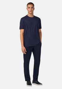 Tamsiai mėlynas trumpų rankovių marškinėliai, pagaminti iš minkštos medžiagos, derinami su atitinkamomis tamsiai mėlynomis kelnėmis, kurios turi lygią tekstūrą ir pritaikytą siluetą, vilkimos su juodomis sportinėmis bateliais.