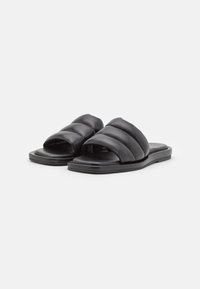 Sandales noires à glissière avec une partie supérieure rembourrée comportant trois sections horizontales, semelle plate et design ouvert à l'avant. Fabriquées en cuir lisse.