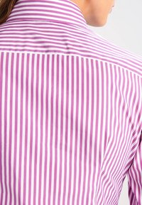 Pruhovaná košile s vertikálními růžovými a bílými pruhy, s klasickým límcem a hladkou tkaninou. Zadní pohled zdůrazňuje design.