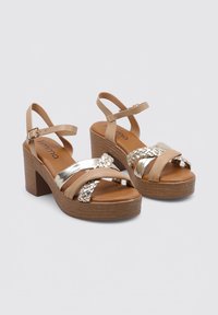 Sandalias de plataforma beige con correas trenzadas, acentos metálicos y un chunky de madera. Correas de tobillo ajustables para un ajuste seguro.