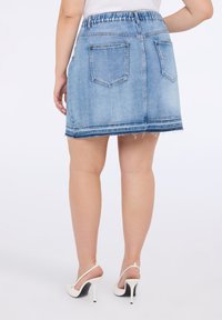 Rok mini denim berwarna biru muda dengan tepi yang tidak rapi, waistband elastis, dan dua saku belakang. Dipadukan dengan sepatu hak tinggi putih.
