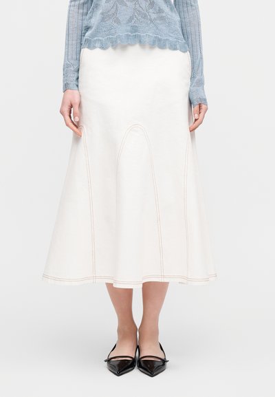 Jupe trapèze blanche en denim avec des coutures contrastantes orange, dotée d'une taille haute et d'un bas évasé, assortie à des chaussures noires à bouts pointus.