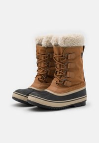 Bottes isolées marron avec une tige en tissu texturé, bordure en fausse fourrure et capuchon en caoutchouc à l'avant. Caractéristiques de cinq boucles de laçage, semelles sombres et accents beiges.