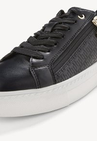 Baskets en cuir noir avec lacets noirs, fermeture éclair latérale, motif géométrique sur la partie latérale, et semelle épaisse en caoutchouc blanc.