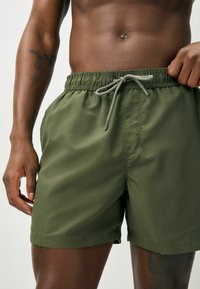 Rohelised ujumispüksid elastse vöökohaga, reguleeritava nööriga, küljetaskutega ja siledast materjalist. Omavad korralikku ääristust ja minimalistlikku disaini.