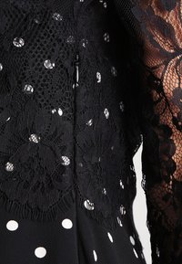 Svart klänning med en spetslinning som har blommönster, prickig tyg och en diskret dragkedjedetalj bak.