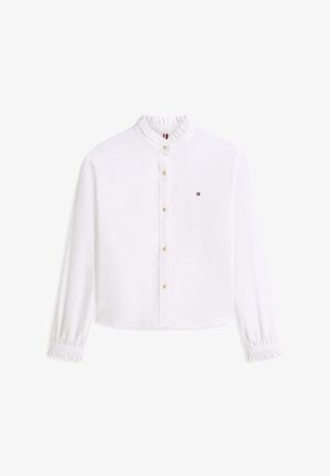 Blusa blanca de manga larga con cuello y puños con volantes, botones dorados en la parte delantera y pequeño logo de Tommy Hilfiger en el pecho izquierdo.
