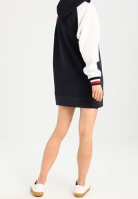 Navyblaues und weißes Kapuzensweatkleid mit roten Streifenakzenten, aus weichem Stoff gefertigt, mit einer Kängurutasche und einem lässigen Schnitt.