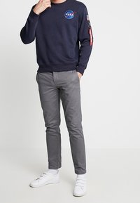 Felpa a girocollo navy con logo NASA, abbinata a chinos slim-fit grigi e sneakers bianche, con etichetta rossa sulla manica.