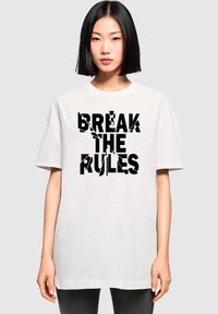 Valge ülikergete lühikeste varrukatega T-särk, millel on boldsete mustade tähtedega tekst "BREAK THE RULES" ning fragmentaarne disain.